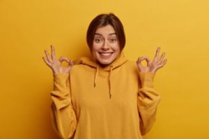 glad dark haired young woman says sounds good confirms something everything control going great approves promo has glad expression agrees with person wears yellow sweatshirt